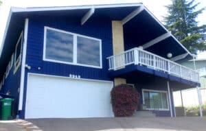 Exterior of a house painted by NE Portland Painters with rich blue siding and white trim and garage door
